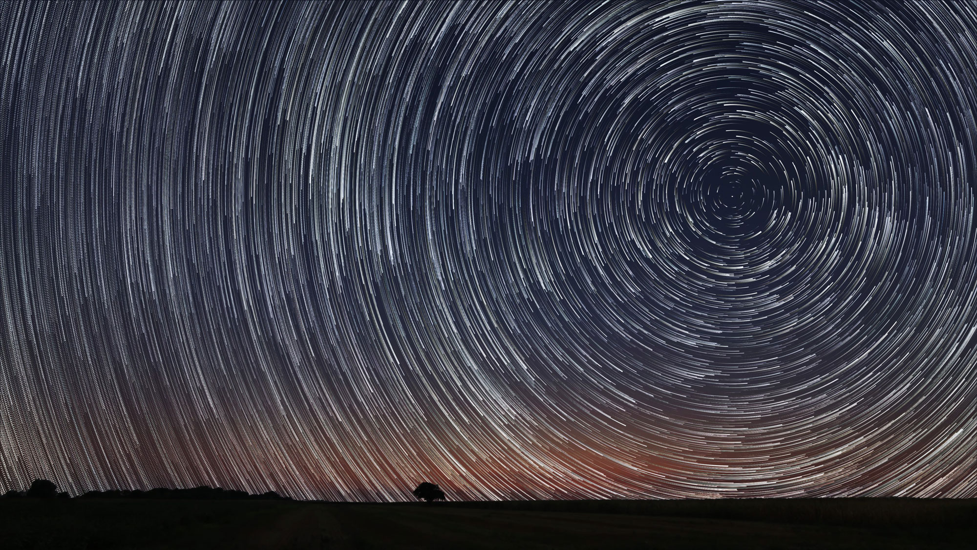 Due to Earth's rotation, the sun, moon, and stars appear in different places in the sky each day. Here, the apparent motion of the stars results in a unique glow across the night sky.