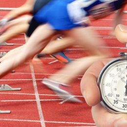 hand holding a stopwatch with runners in the background