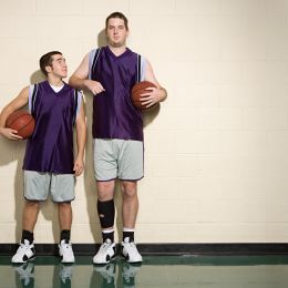 tall basketball player standing next to shorter player in purple jerseys