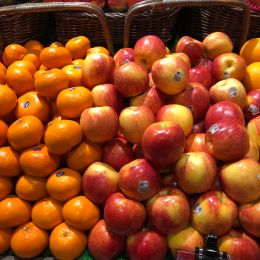 large stacks of apples and oranges in baskets in a market
