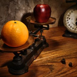 apple and orange on a scale on a brown wooden table