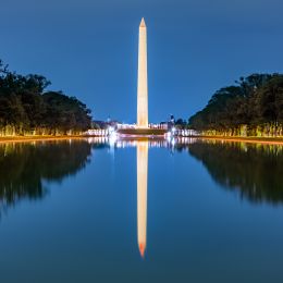tall washington monument reflecting in water in the evening