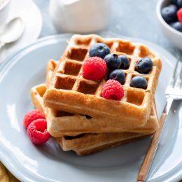 stack of waffles with berries on top on a white plate with a fork